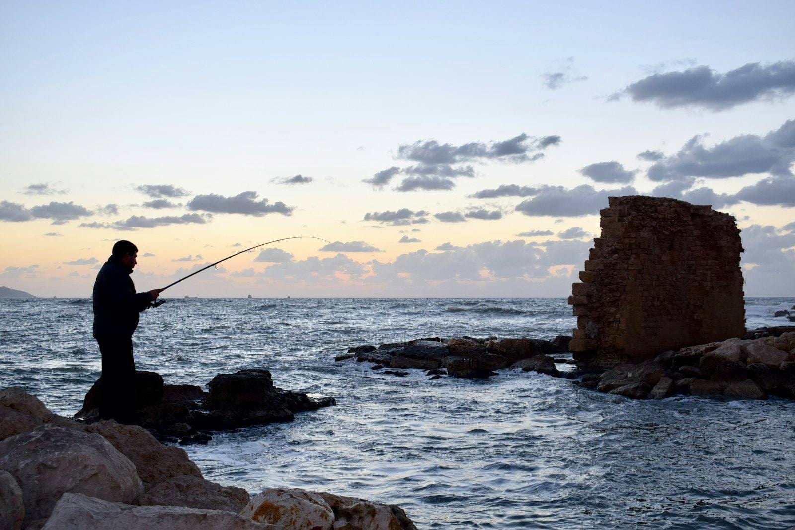 An angler in silhouette on the rocks at dusk, rod bent as he casts out over the sea