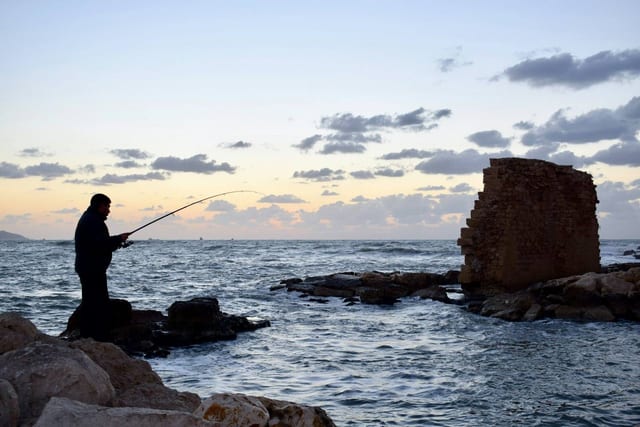 An angler casting from the rocks beside an old stone tower at dusk