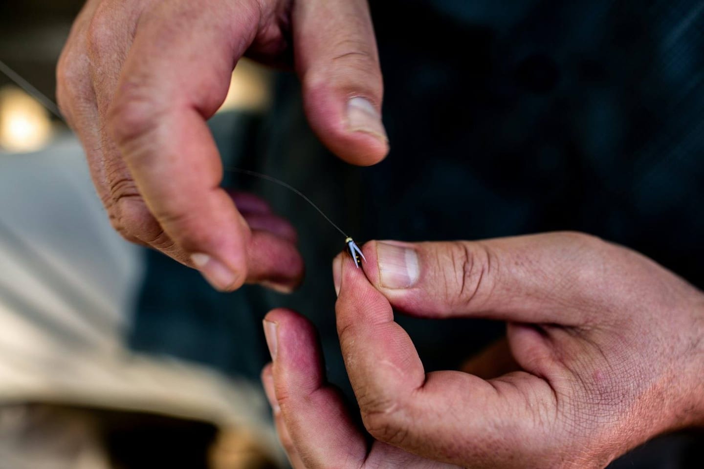 Hands tying a hook onto fishing line
