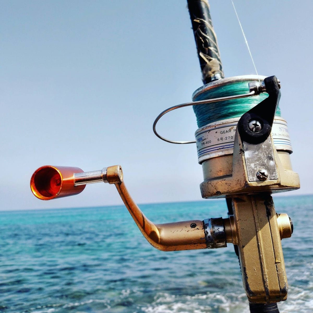 A spinning reel loaded with green line, against blue sky and sea